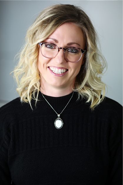 A woman wearing glasses and a necklace is smiling for the camera.