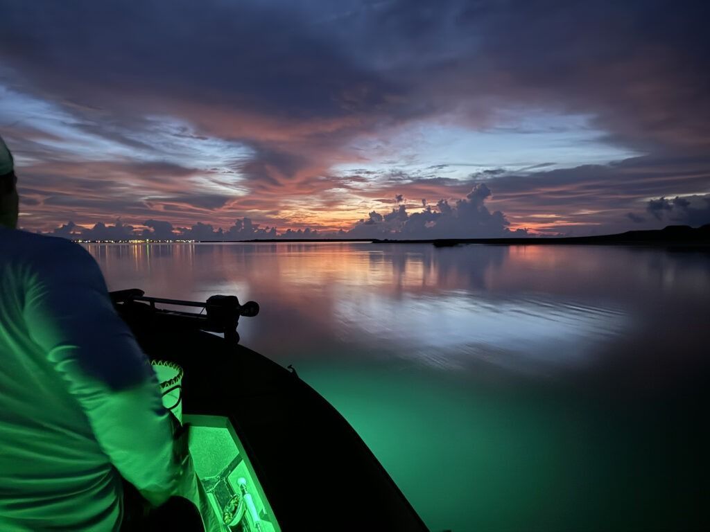A man is sitting on a boat in the water at sunset.
