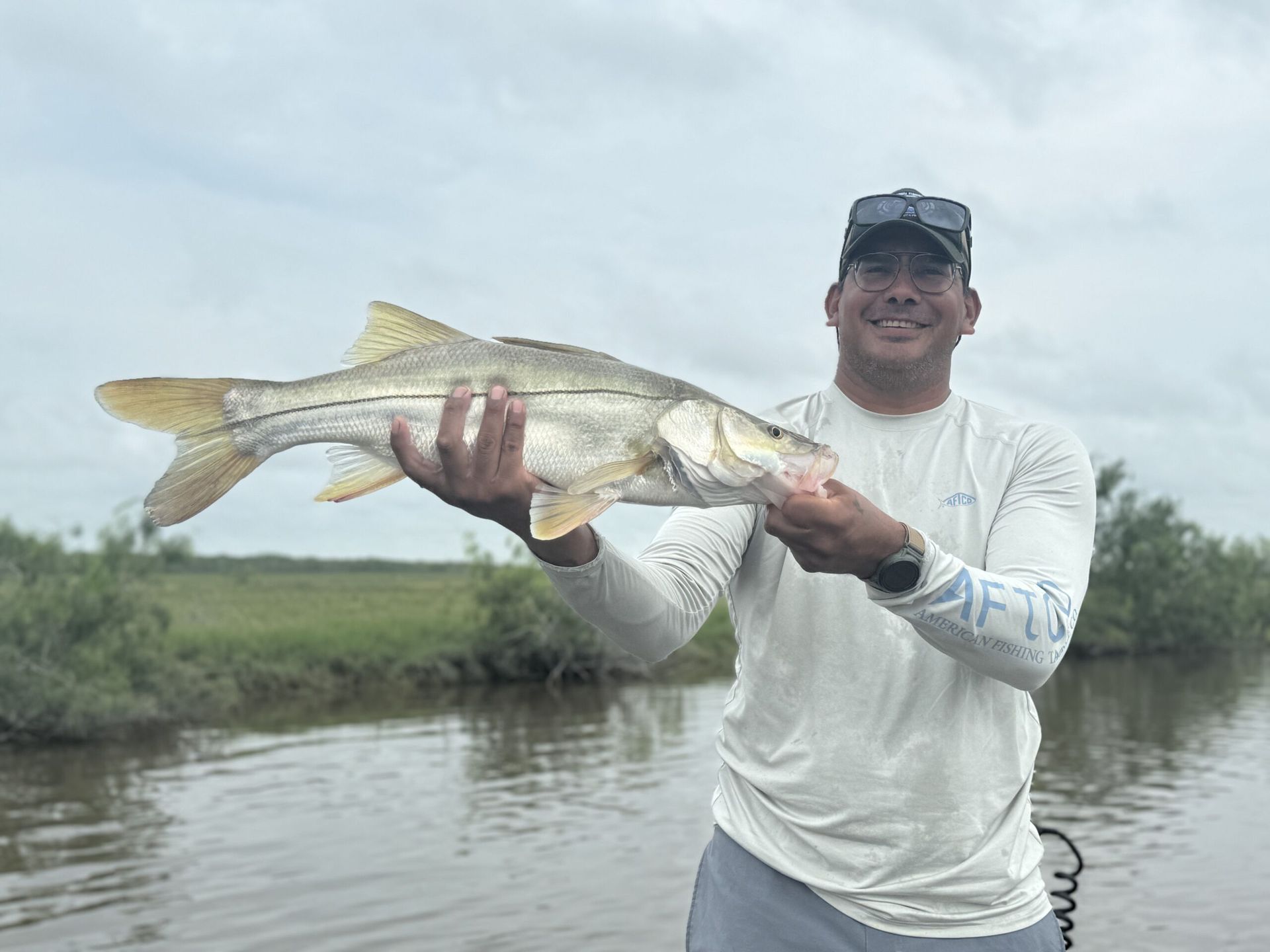 A man is holding a large fish in his hands in front of a body of water.