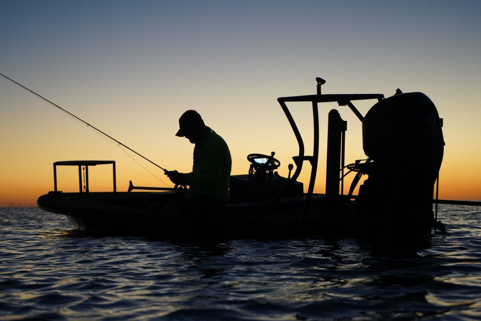 A man is fishing in a boat at sunset