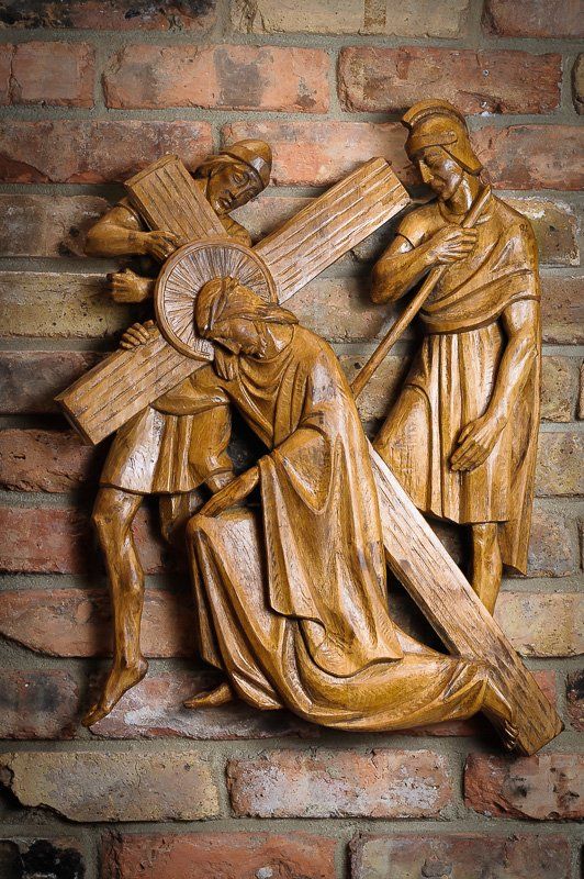 a wood carving of jesus carrying a cross on a brick wall