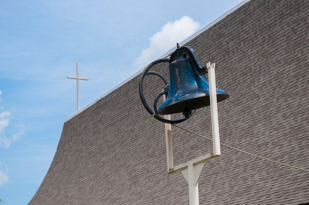 a church bell on a pole with a cross in the background