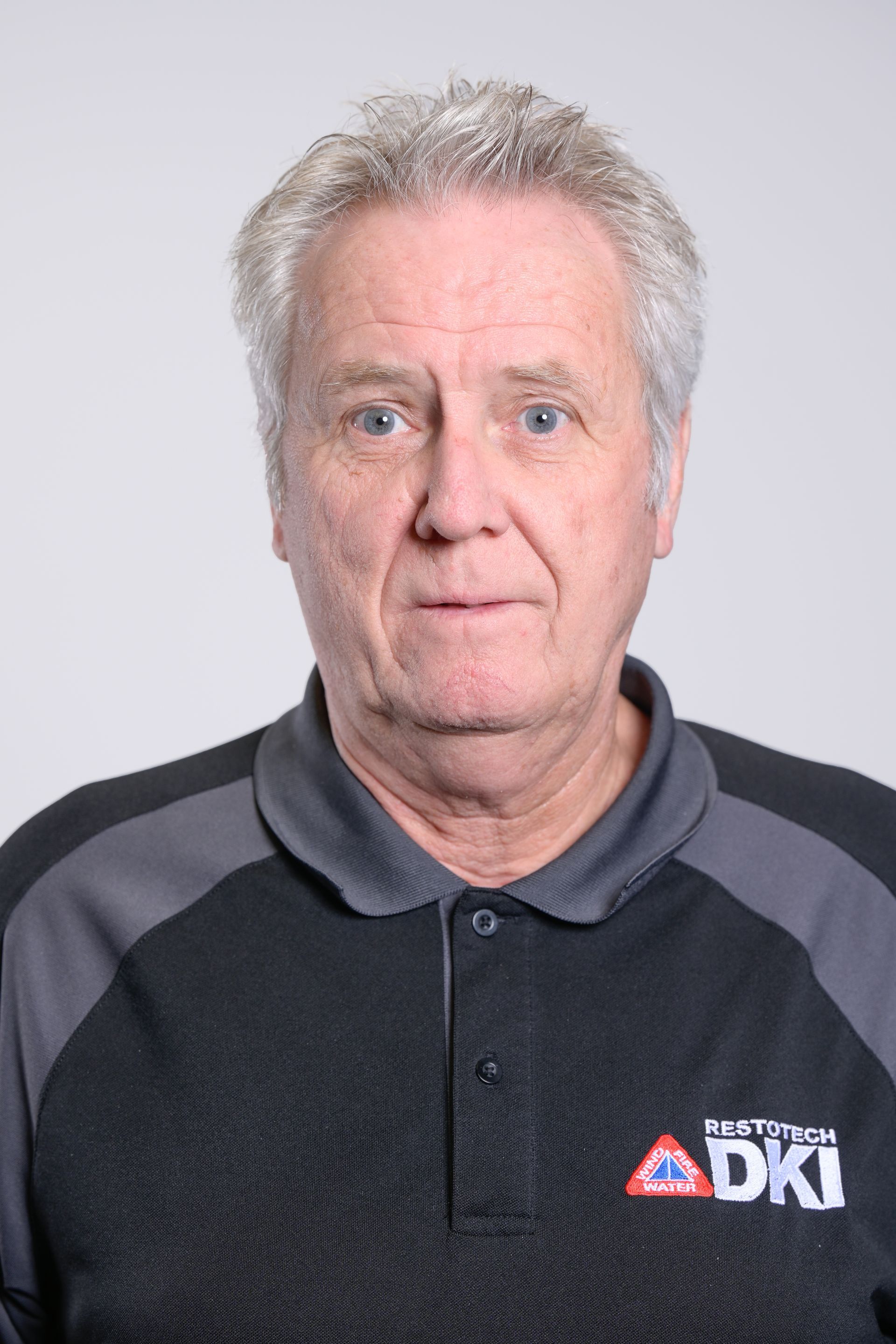 Man in a black and gray shirt looking at the camera. He has gray hair and a neutral expression.