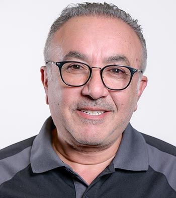 Man wearing glasses smiling, gray shirt, against a white background.
