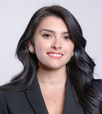 Woman with dark hair smiles, wearing a black blazer, necklace, and earrings.