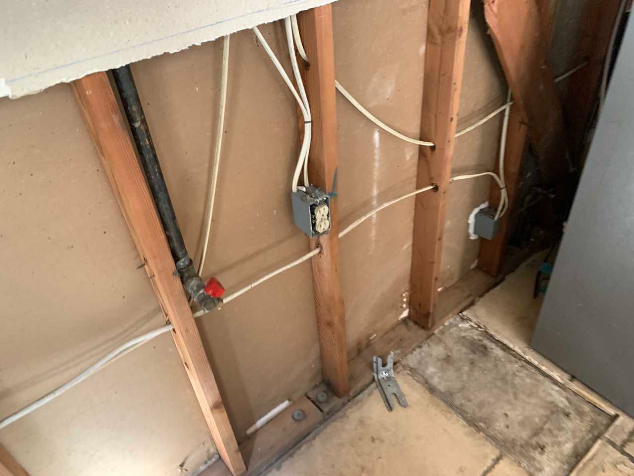Interior wall with exposed studs, electrical wiring, gas pipe, and an electrical outlet box.