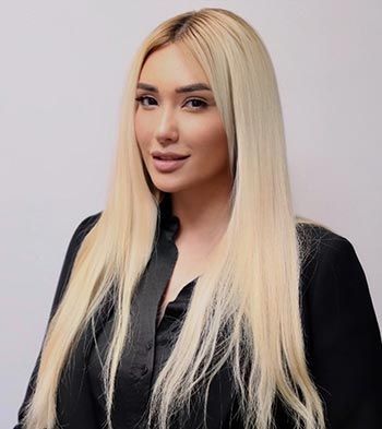 Woman with long blonde hair, wearing a black shirt, smiles.
