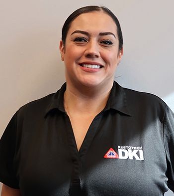 Woman in black polo shirt smiles, wearing a company logo.