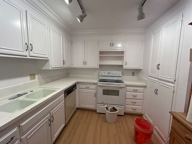 White kitchen with cabinets, stove, sink, and light-colored countertops and flooring.