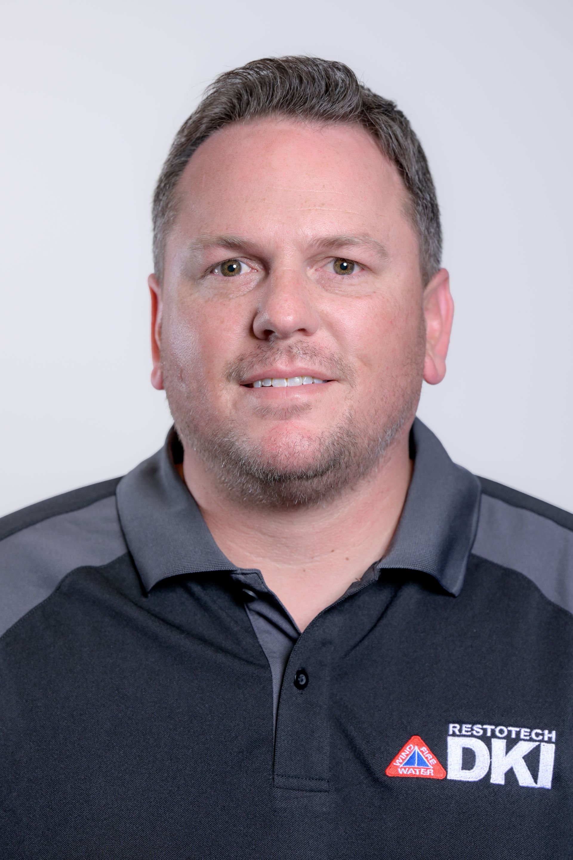 Man with short brown hair, wearing a black and gray polo shirt with a company logo.