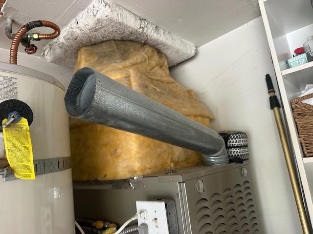 Furnace with metal vent pipe; water heater to left. Insulation covers area above the furnace.