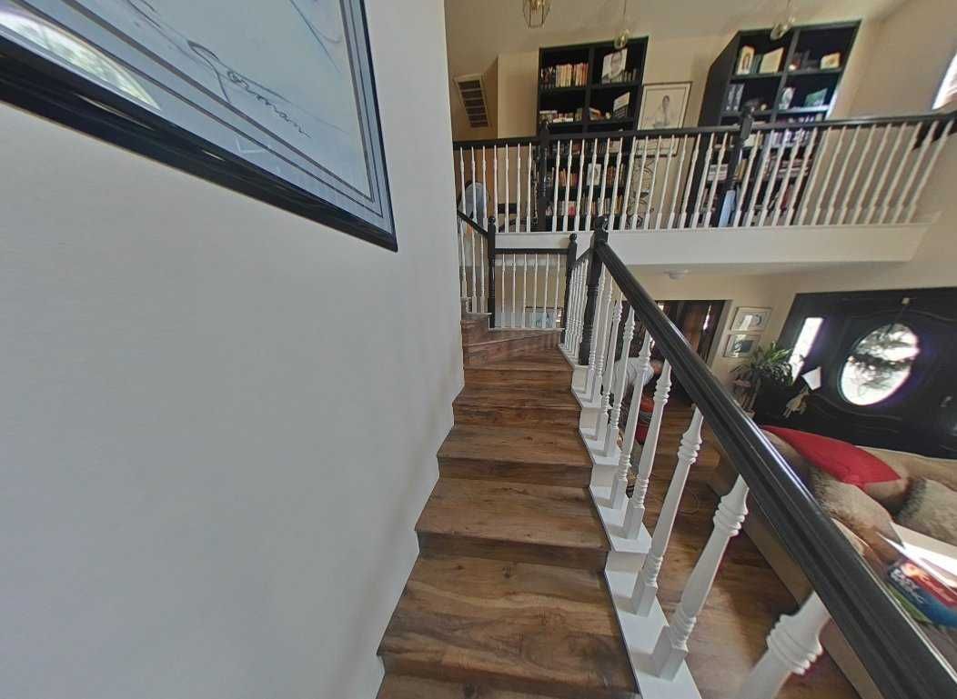 Wooden staircase leading up to a second-floor balcony with a railing. The railing is black and white.