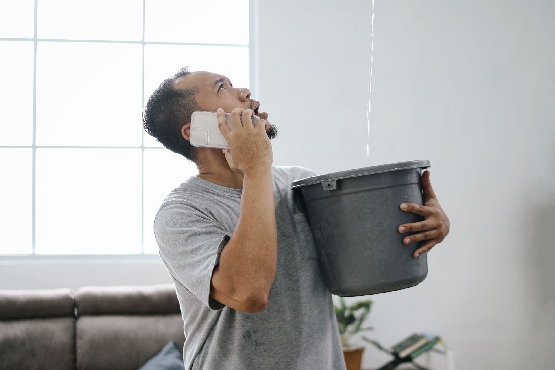 Man holding bucket to catch water leaking from ceiling