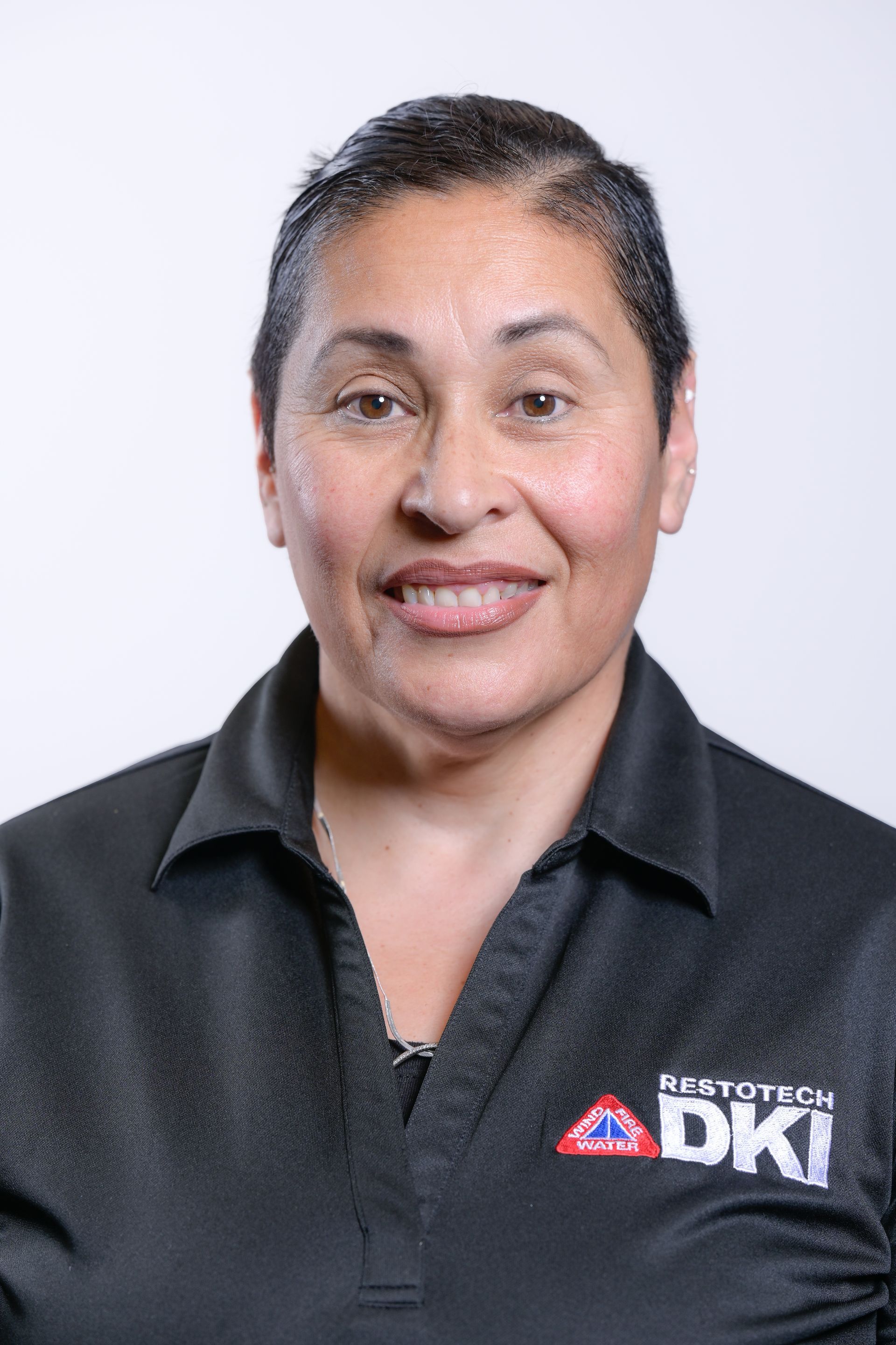 Woman wearing a black polo shirt smiles. Logo on the shirt reads 