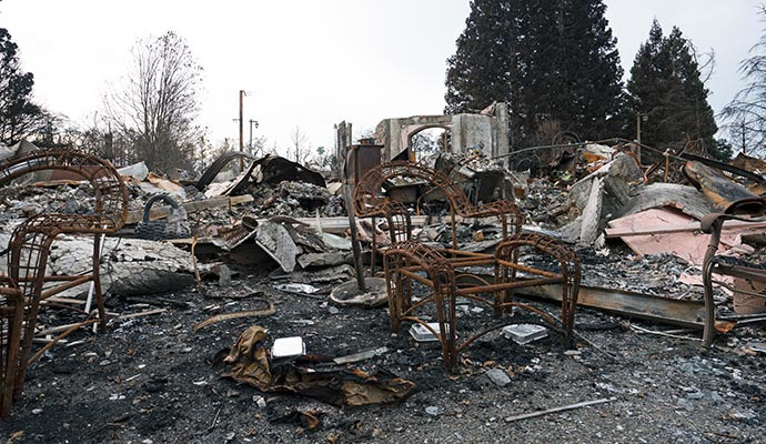 Charred remains of a structure, including furniture, amidst rubble and ash.