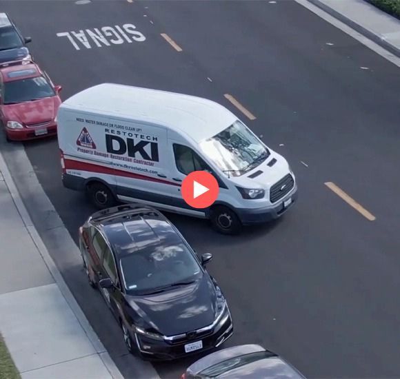 White DKI van parked on road with other vehicles near a sidewalk.