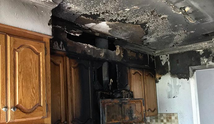 Kitchen cabinets and ceiling damaged by fire, charred and blackened.