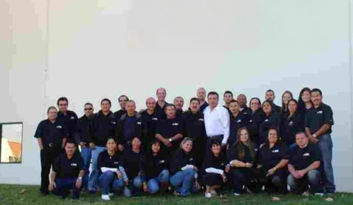 Group of people in black shirts posing in front of a white wall. Some are kneeling.