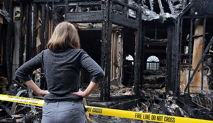 Woman looking at a burned-out house, hands on hips, yellow
