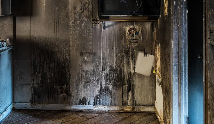 Room with charred walls and ceiling, a broken TV, and a door, likely damaged by fire.