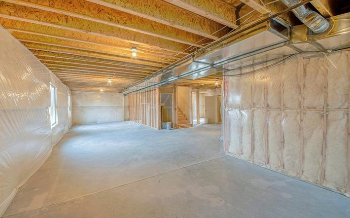 Unfinished basement with concrete floor, insulation, exposed wooden beams, and ductwork.