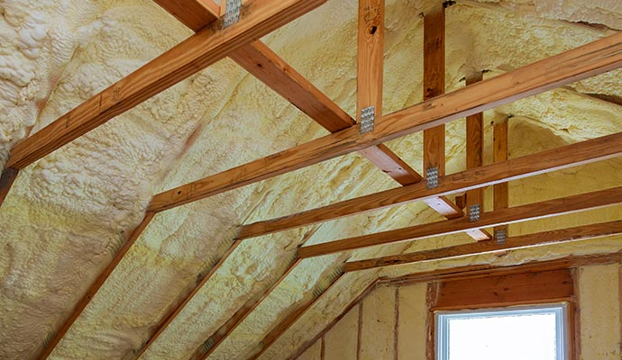 Attic rafters coated with yellow spray foam insulation.