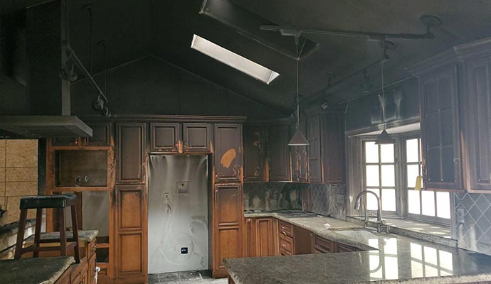 Charred kitchen interior, walls and cabinets damaged by fire; skylight visible.