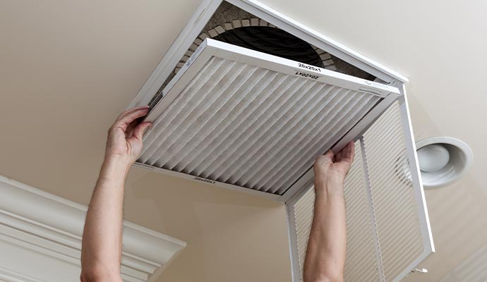 Person replacing an air filter in a ceiling vent.