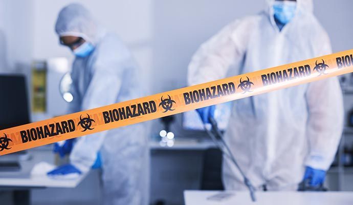 Two people in hazmat suits cleaning a lab; orange biohazard tape in the foreground.