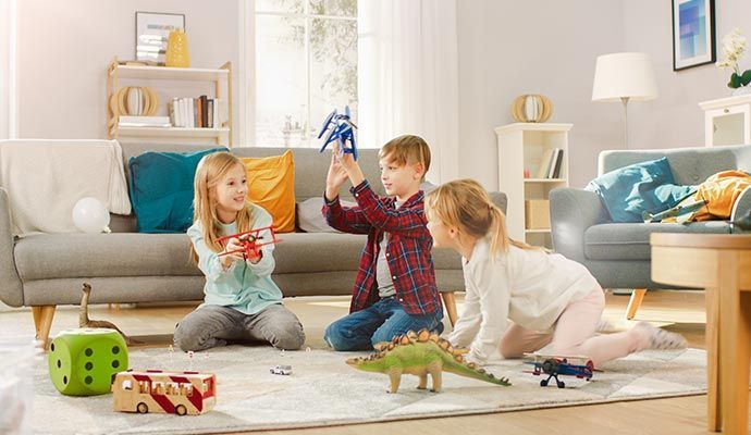 Three children playing with toys on a rug in a living room.