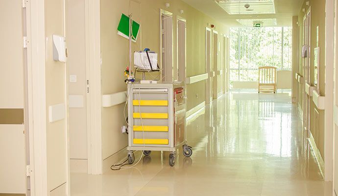 Hospital hallway with medical cart, handrails, and a chair near a window.