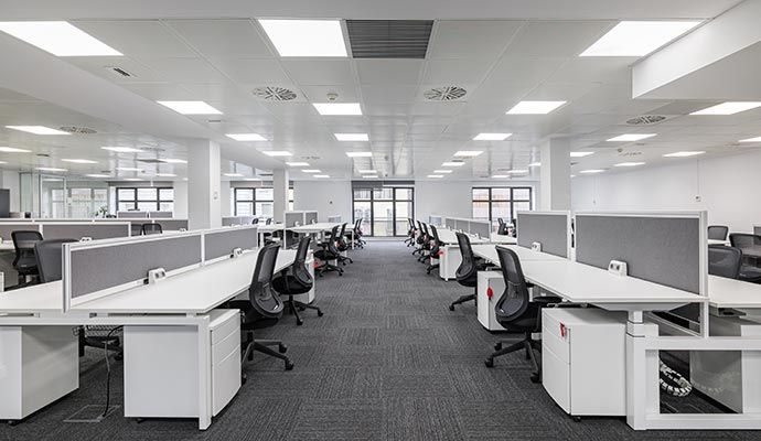 Modern office space with rows of white desks, gray partitions, and black chairs.