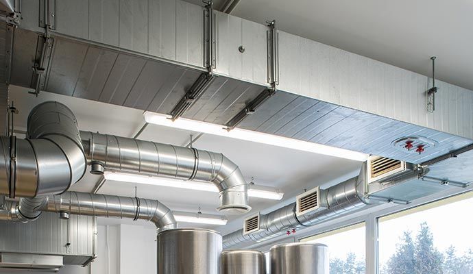 HVAC system in a commercial setting: ductwork, vents, and lighting fixtures against a white ceiling.