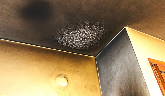 Ceiling and wall corner damaged by fire, with soot and discoloration.