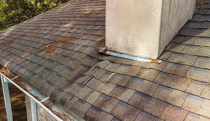 Damaged asphalt shingle roof with a chimney; brown and gray hues, with debris.