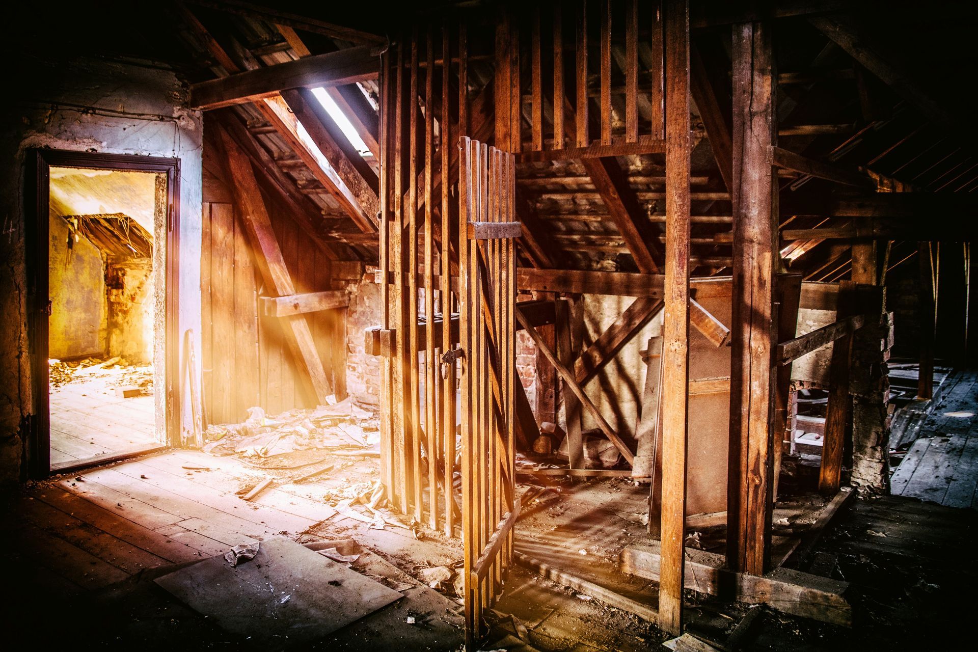 Dilapidated attic interior with wooden beams and a doorway, illuminated by light.