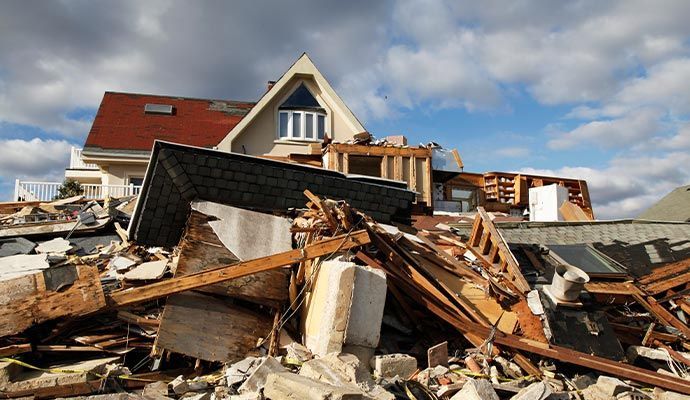 House severely damaged; debris in foreground; red roof; blue sky.