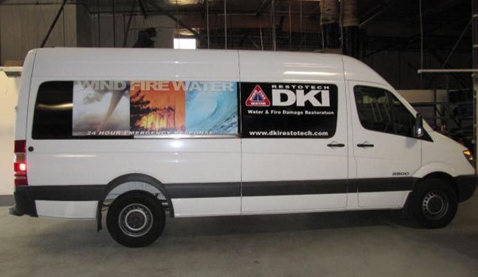 White van with DKI logo, advertising wind, fire, and water damage restoration services.