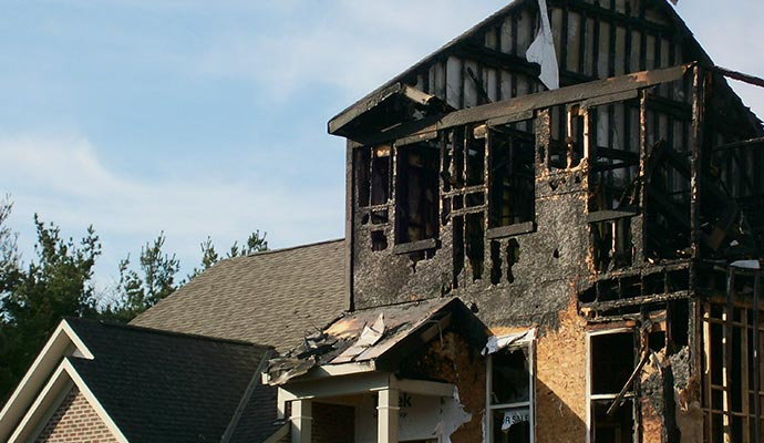 Burnt remains of a two-story house after a fire, with charred wood frame and exposed interior.