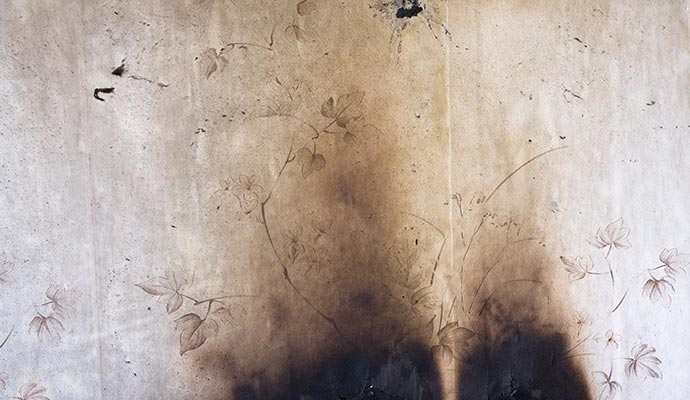 Damaged wallpaper with dark burn marks and faint floral pattern.