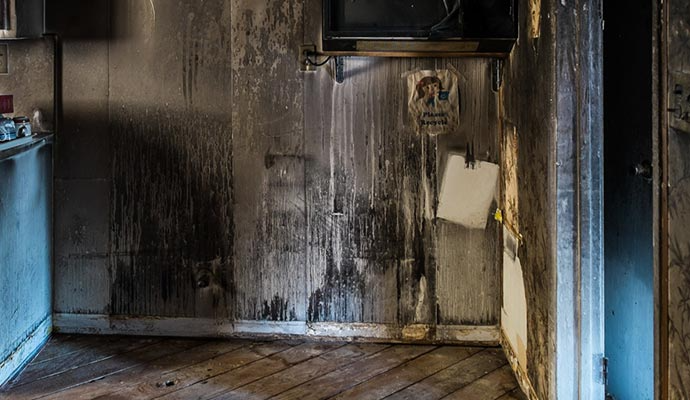 Interior of a fire-damaged room with charred walls, debris, and burnt wood flooring.