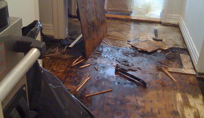 Damaged wooden floor with debris and tools, likely during repair or demolition.