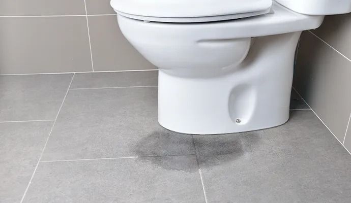 A toilet on a tiled floor with a dark water stain.