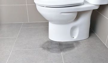 Toilet on grey tiled floor with a water stain beneath it.