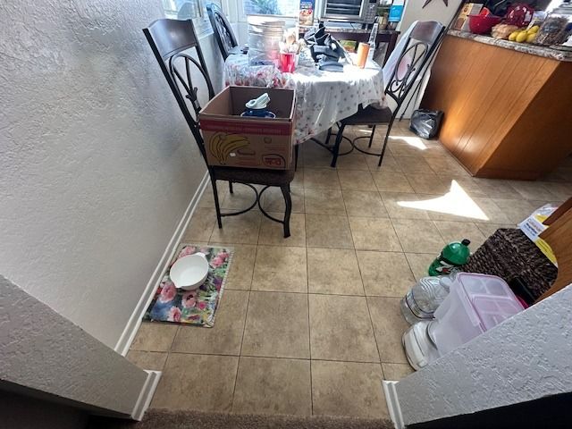 A kitchen interior with a table, chairs, a box on a chair, and various items on the floor.