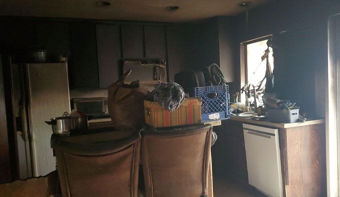 Fire-damaged kitchen interior; charred cabinets, appliances, and debris visible.
