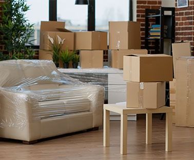 Moving boxes stacked in a room with wrapped furniture.