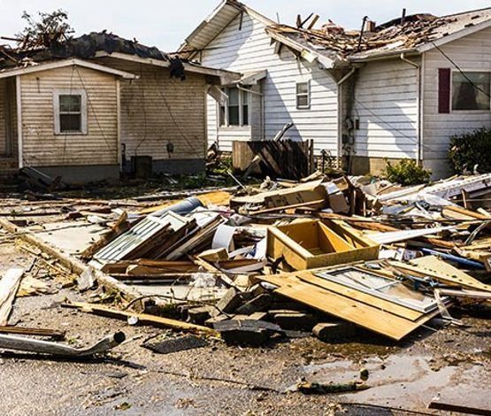 Debris and damaged houses after a storm. Wooden fragments litter the ground. Buildings have missing roofs.