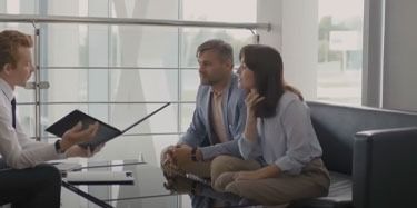 A man presenting documents to a couple seated on a couch in a bright office setting.