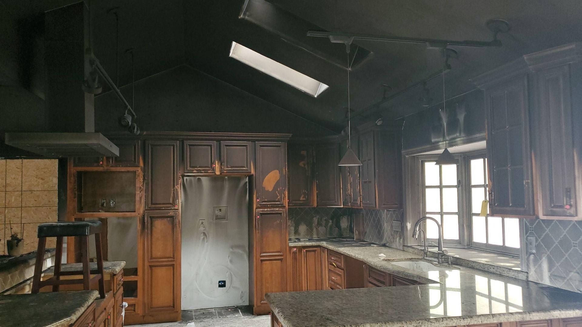 Fire-damaged kitchen: burnt cabinets, ceiling, and appliances. Smoke-stained walls. Skylight.